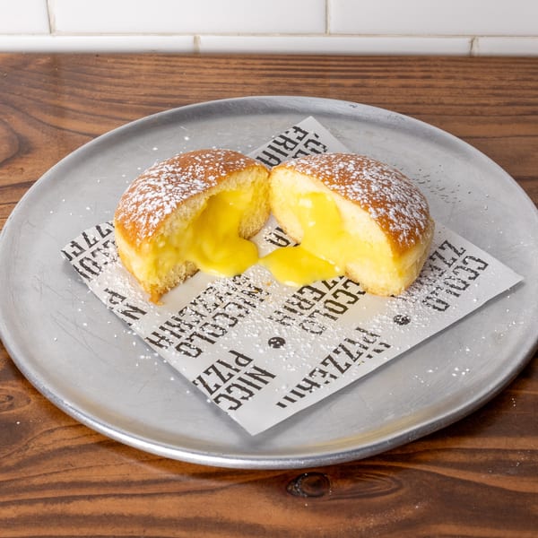 A powdered sugar-dusted pastry, split open to reveal a creamy yellow filling, on a metal plate.