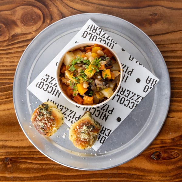 Hearty vegetable stew with white beans and herbs, served with two garlic knots on a metal tray.