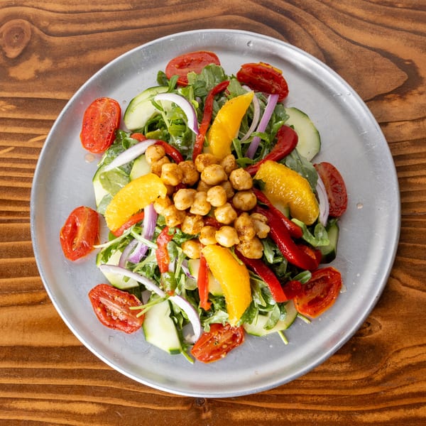 Colorful salad with chickpeas, roasted tomatoes, cucumbers, red onion, and orange segments on a metal plate.