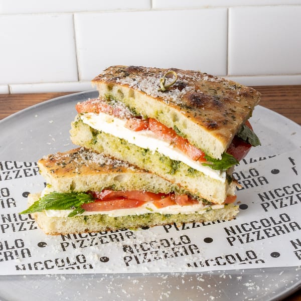 Two halves of a focaccia sandwich with pesto, mozzarella, and tomatoes on a metal tray.