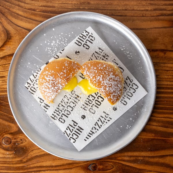 Two powdered sugar-dusted pastries, split open to reveal a creamy yellow filling, on a metal plate.