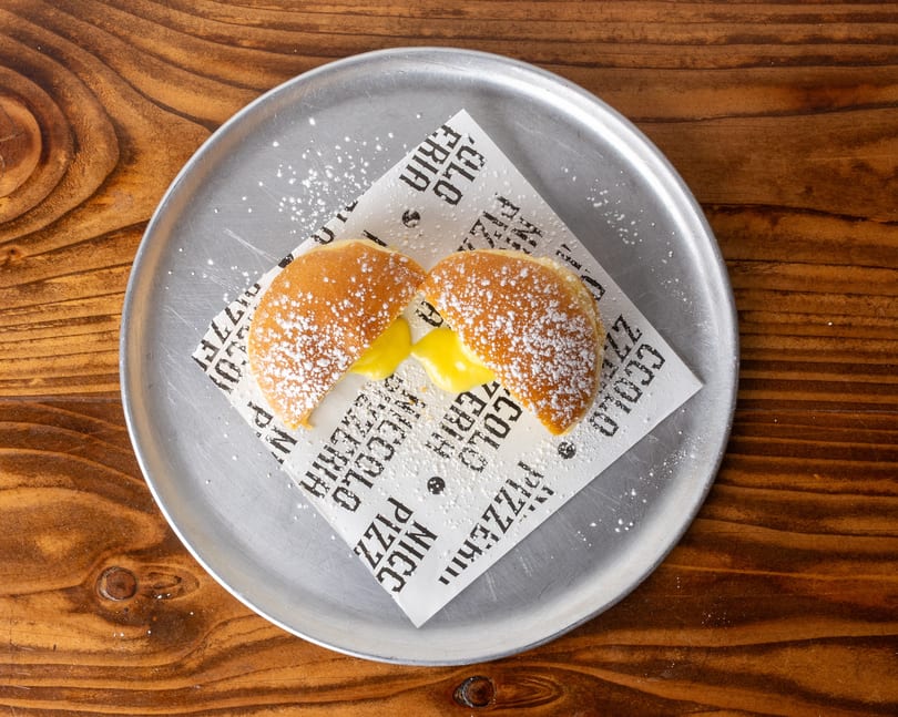 Two powdered sugar-dusted pastries, split open to reveal a creamy yellow filling, on a metal plate.