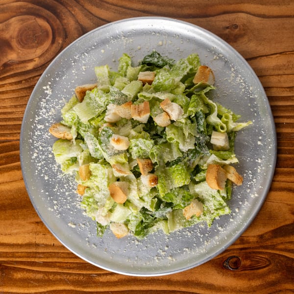 Overhead view of a Caesar salad with romaine lettuce, croutons, and parmesan cheese on a metal plate.