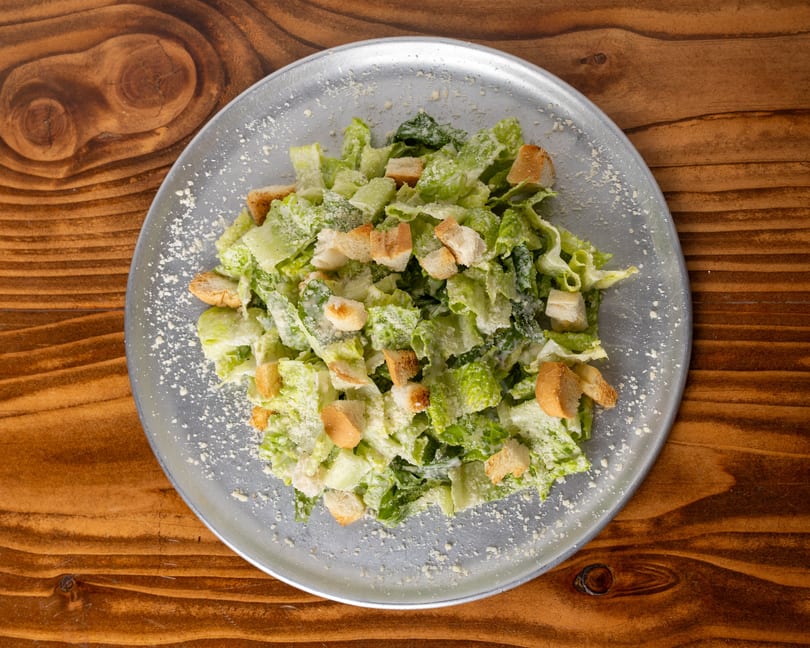 Overhead view of a Caesar salad with romaine lettuce, croutons, and parmesan cheese on a metal plate.