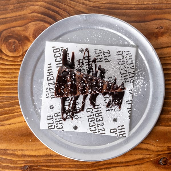 A chocolate brownie slice with chocolate drizzle and powdered sugar on a metal plate.