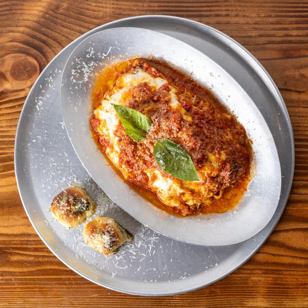 Baked lasagna with rich red sauce, melted cheese, fresh basil, and two garlic knots on a metal tray.