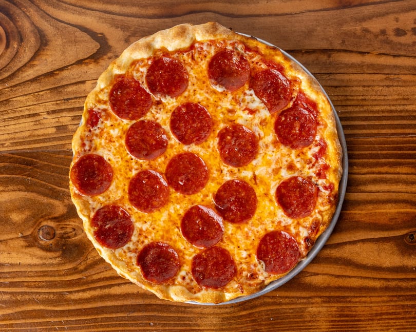 A freshly baked pepperoni pizza with a golden crust sits on a rustic wooden table.